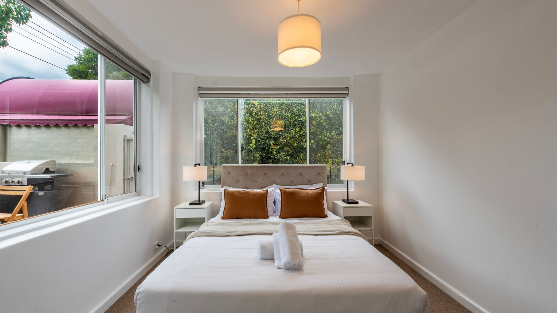 Habitación de hotel con cama, dos lámparas de noche, una ventana con vista a follaje e iluminación en el techo.