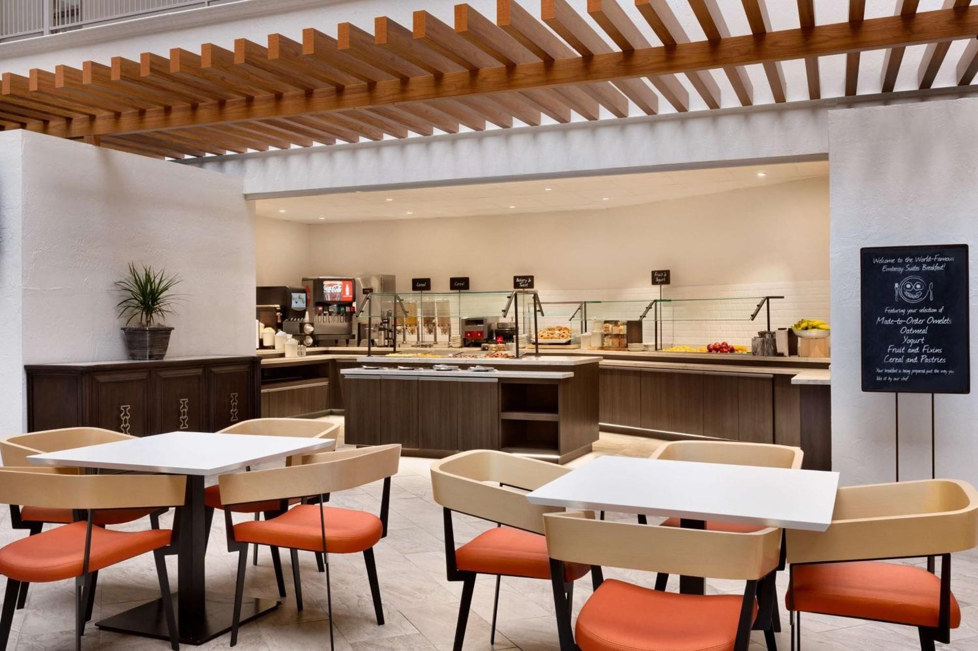A modern breakfast area with tables and chairs, a coffee machine, and a sign indicating the breakfast menu.
