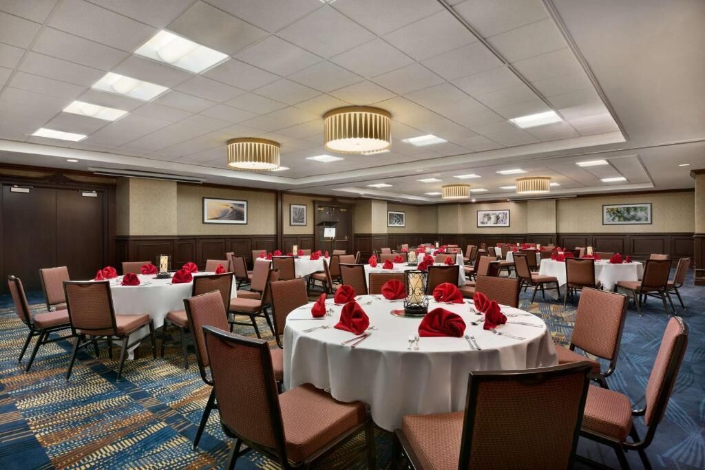 A conference room with round tables, chairs, and red napkins.