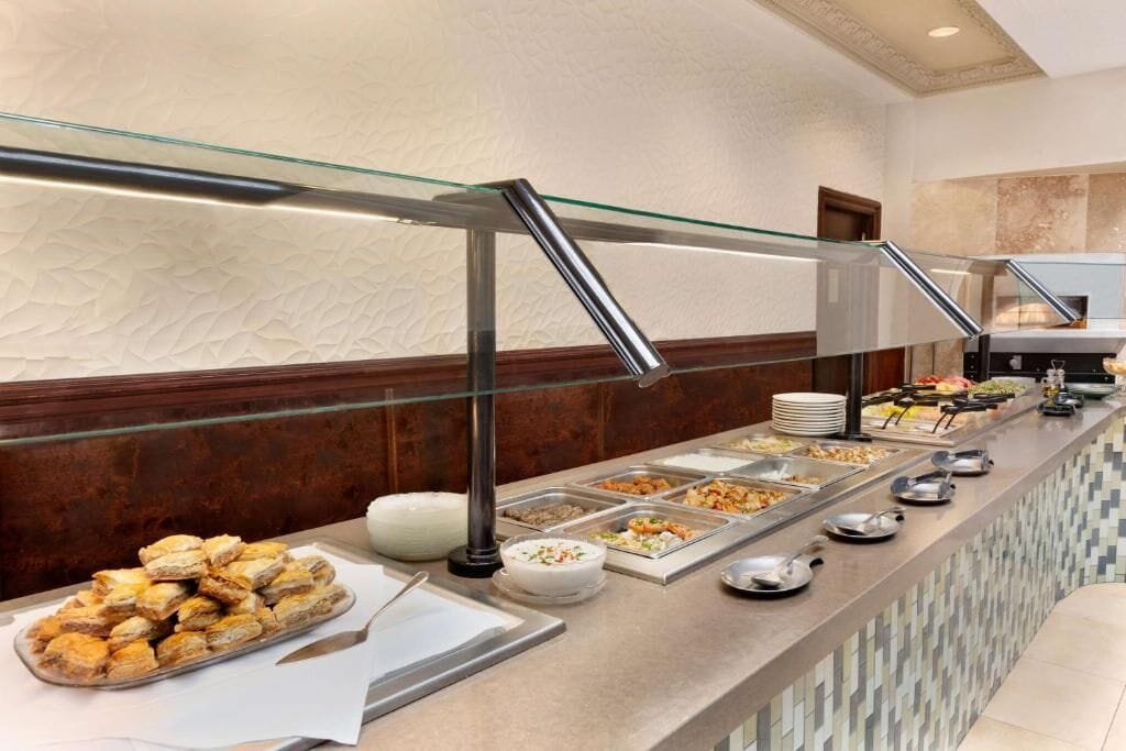 A buffet area with various food options, a glass railing, and a tiled backsplash.