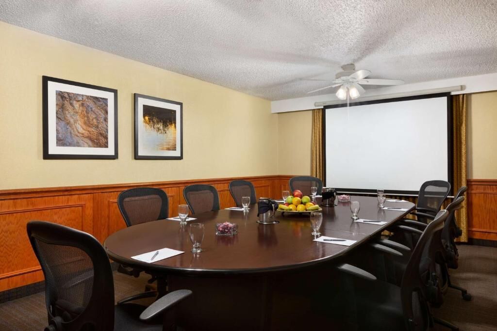 Una sala de conferencias con una gran mesa, sillas, una pantalla de proyector y cuadros en la pared.