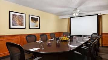 Una sala de conferencias con una gran mesa, sillas, una pantalla de proyector y cuadros en la pared.