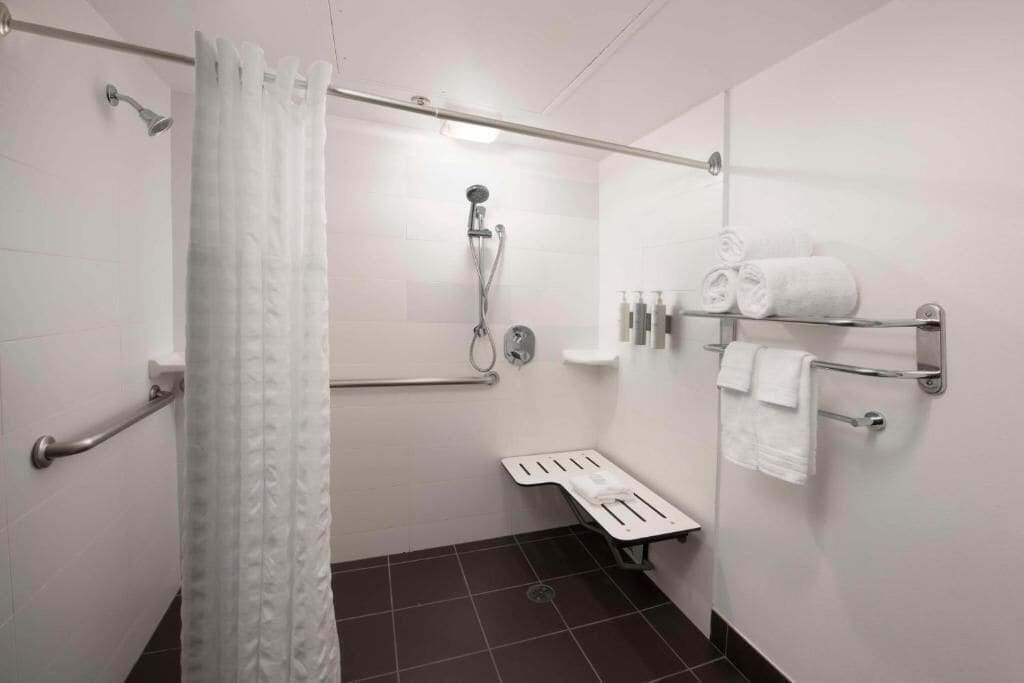 A modern bathroom with a shower, grab bars, a toilet with a raised seat, and a towel rack with towels.