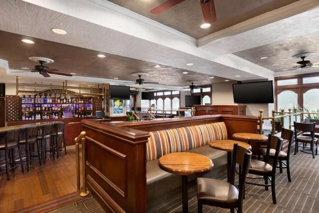 Zona de bar con una barra larga, varios taburetes y un área de estar con banco y mesas.