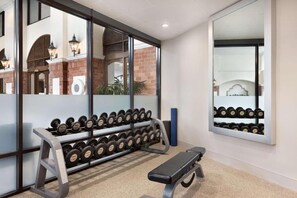 Un gimnasio con banco, mancuernas y espejo.