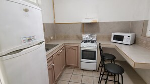 Une cuisine compacte équipée d’un réfrigérateur, d’une cuisinière, d’un four à micro-ondes et de deux tabourets de bar.