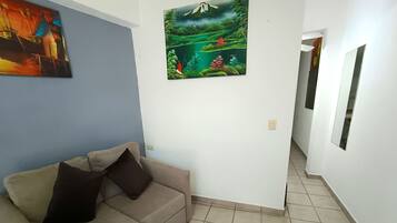 A room with a beige sofa, a painting of a landscape, and a tiled floor.