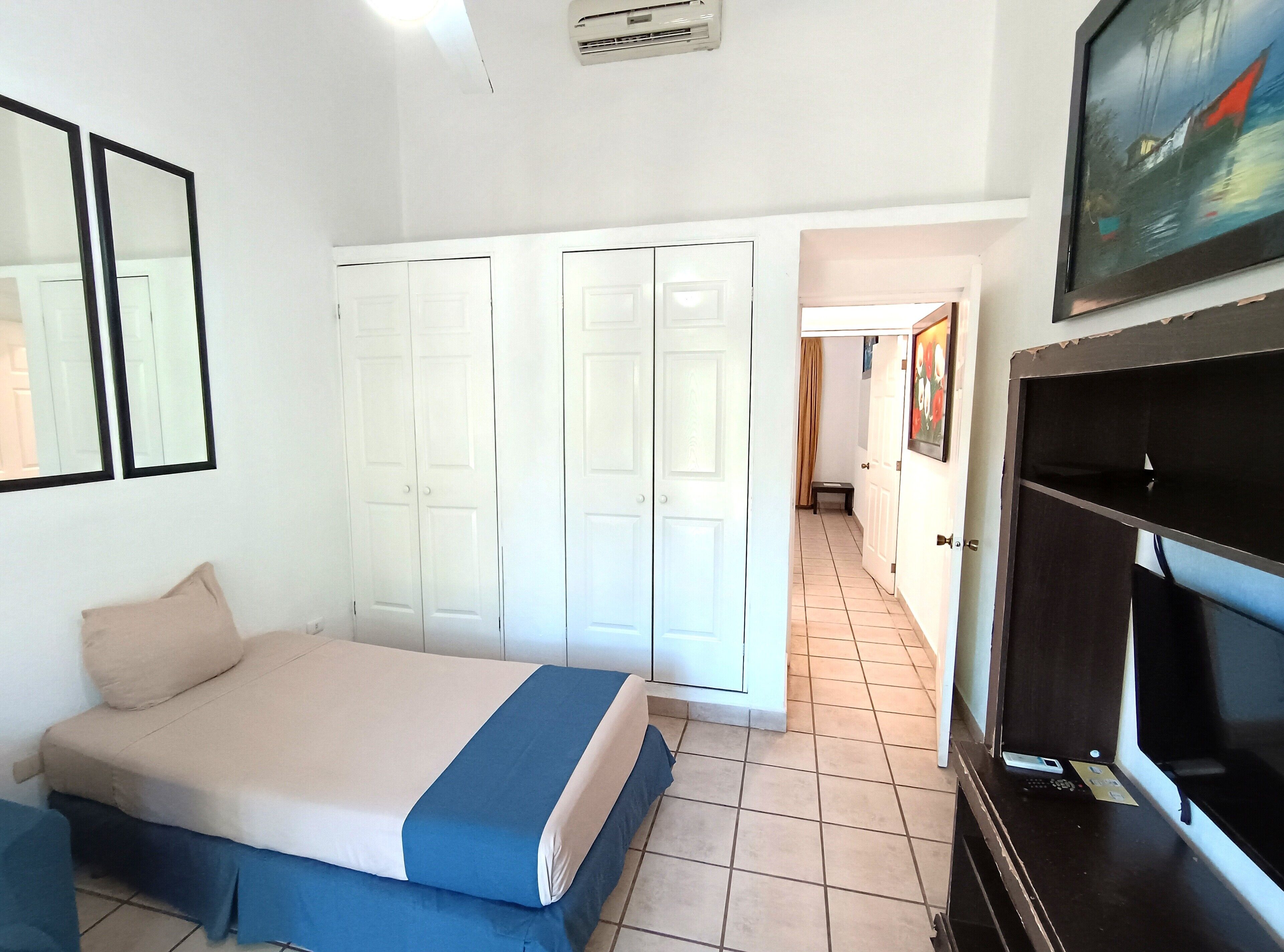 A bedroom with a bed, a wardrobe, a television, and a painting on the wall.