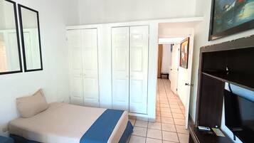 A bedroom with a bed, a wardrobe, a television, and a painting on the wall.
