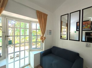 Una habitación con un sofá azul, una ventana con cortinas y un espejo montado en la pared.