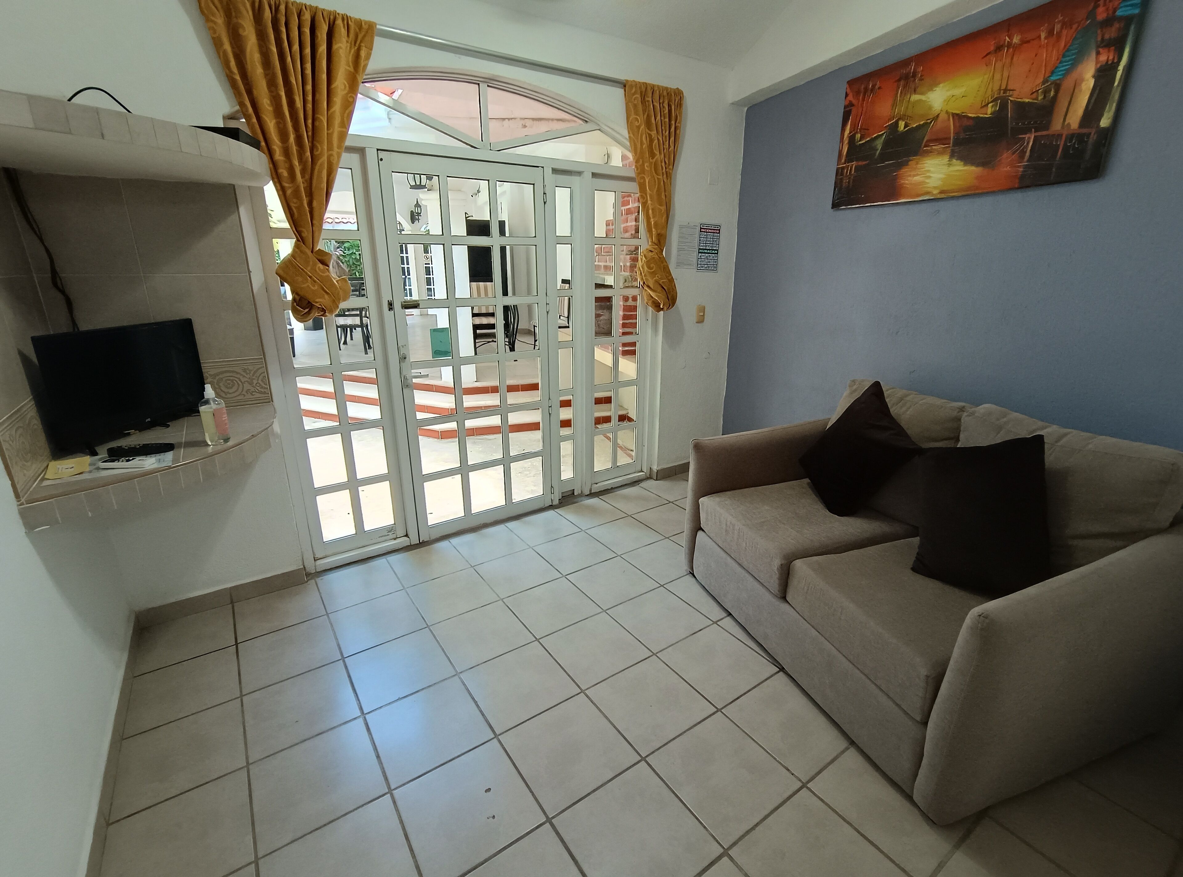 Una habitación con un sofá, una televisión, una puerta con paneles de vidrio y un cuadro en la pared.