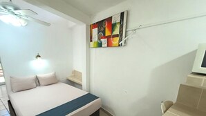 Une chambre d’hôtel avec un lit, un ventilateur de plafond, un téléviseur fixé au mur et une petite table.