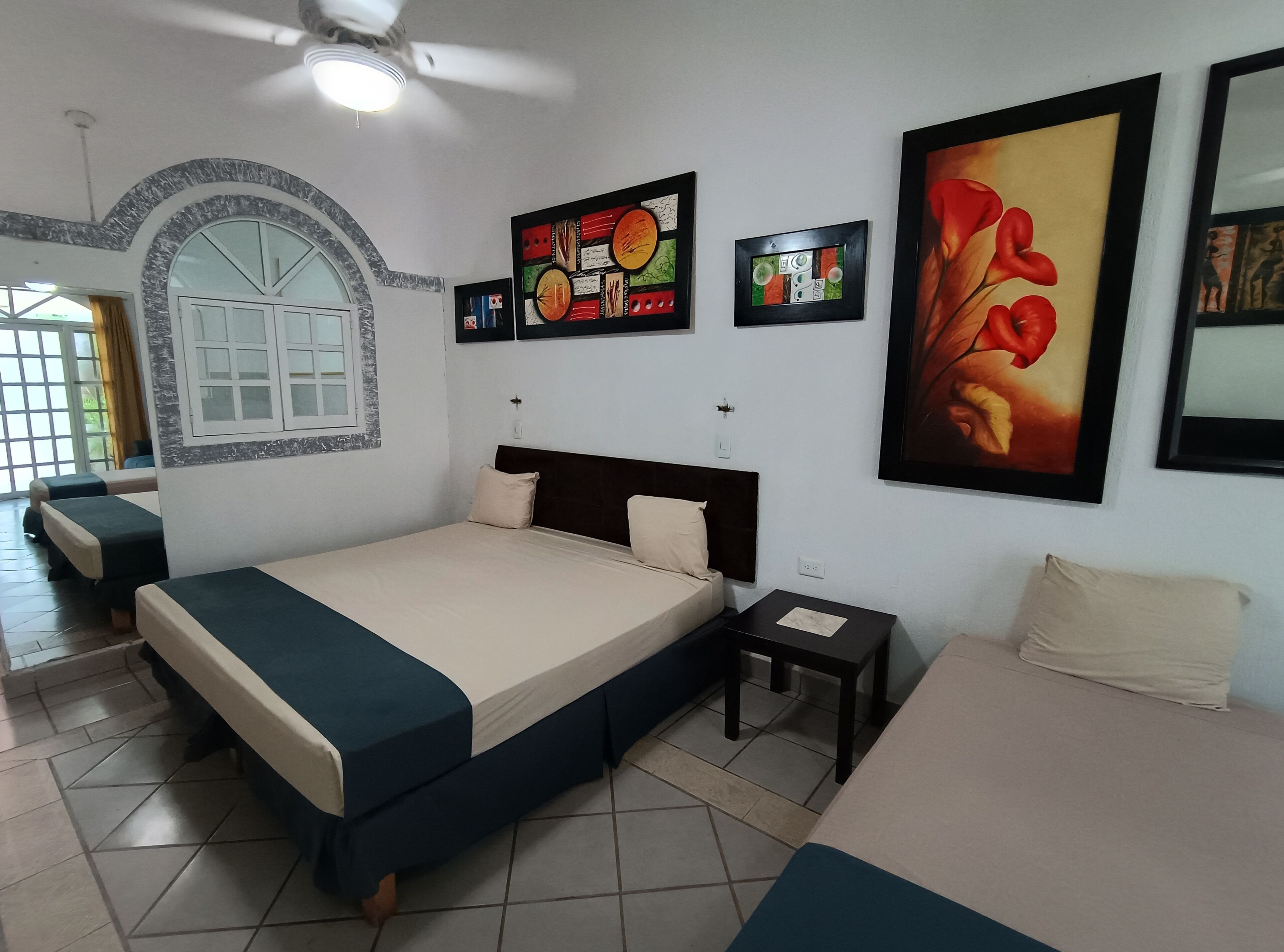 A hotel room with a bed, a nightstand, a chair, a ceiling fan, and artwork on the walls.