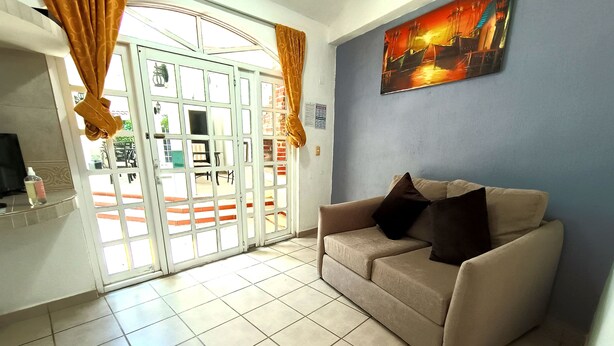 Une pièce avec un canapé beige, un tableau au mur et une porte avec des rideaux.