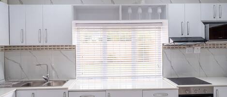 A modern kitchen with white cabinetry, a built-in oven, and a window with blinds.