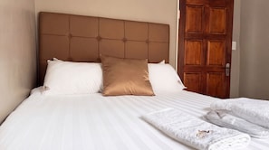 Habitación de hotel con una cama grande, una puerta de madera y una cama bien hecha con sábanas blancas y una almohada marrón.