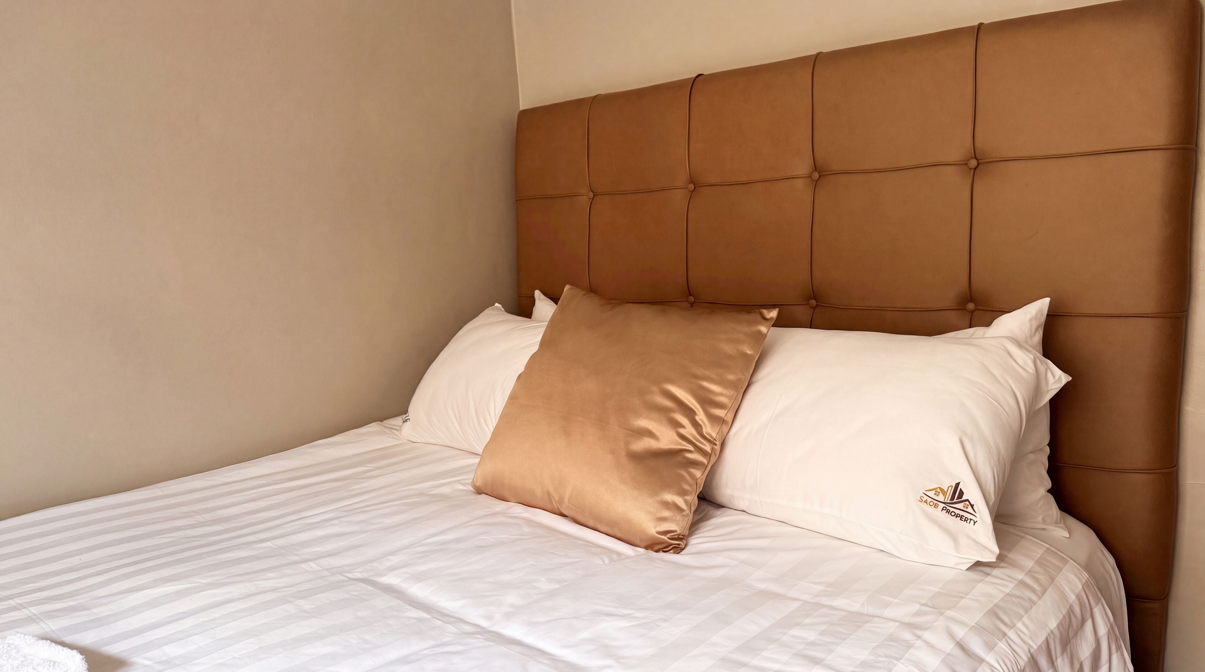 A bed with a tufted headboard, two pillows, and a white bedspread.