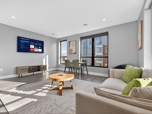 A modern living room with a flat-screen TV, a round wooden coffee table, a beige sofa, and a dining area with chairs and a table. - Spacious 3BR Boston Base | Free Parking (Boston)