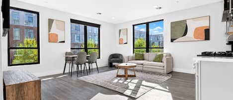 A modern living room with a sofa, chairs, a coffee table, and a kitchen area with a stove.