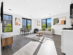 A modern living room with a sofa, chairs, a coffee table, and a kitchen area with a stove.