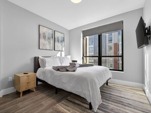 A bedroom with a bed, a nightstand, a window, and a wall-mounted TV. - Spacious 3BR Boston Base | Free Parking (Boston)