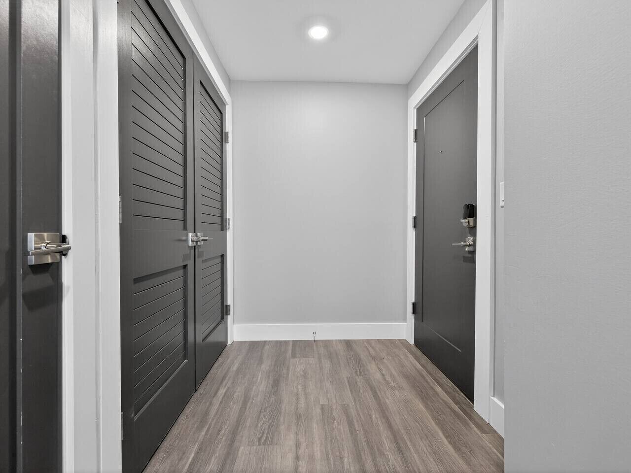 A hallway with two doors, a light switch on the wall, and a wooden floor.
