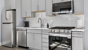 A modern kitchen with stainless steel appliances, white cabinetry, and a tiled backsplash.
