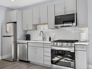A modern kitchen with stainless steel appliances, white cabinetry, and a tiled backsplash.