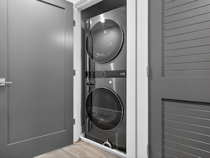 A laundry room with two stacked washing machines, a door, and a wall with horizontal lines.