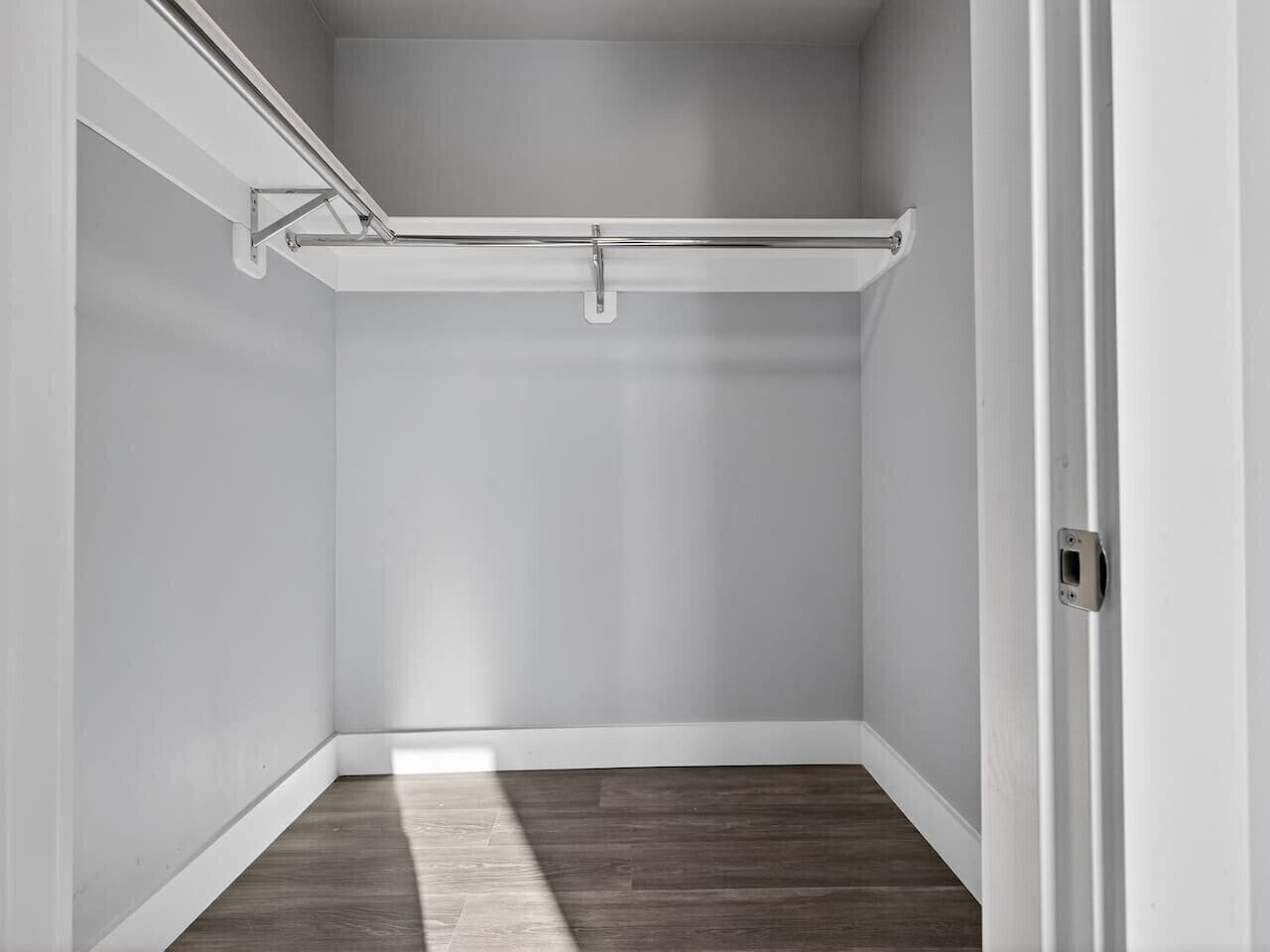 A corner room with a wooden floor, white walls, and a metal ceiling track.