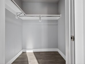 A corner room with a wooden floor, white walls, and a metal ceiling track.