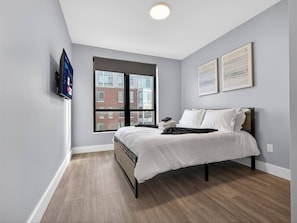 A bedroom with a bed, a window, and a mounted television.