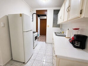 A compact kitchen with a refrigerator, oven, and a coffee maker.