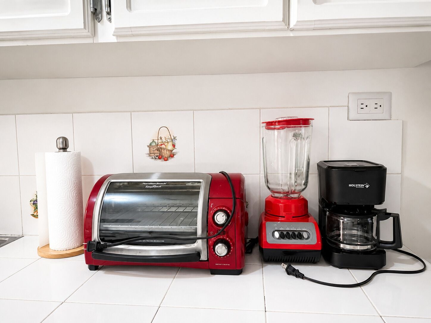 Eine Küche mit einem roten Toaster, einem roten Mixer und einer schwarzen Kaffeemaschine auf einer weißen Fliesenarbeitsplatte.