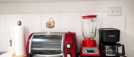 A kitchen with a red toaster, a red blender, and a black coffee maker on a white tiled countertop.