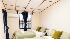 Habitación de hotel con dos camas, una ventana con cortinas, una mesita con lámpara y un control remoto en el suelo.