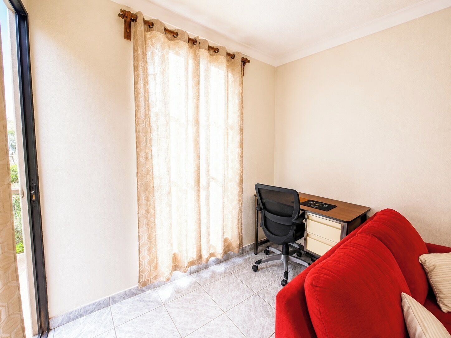 Una habitación con escritorio, silla de oficina y sofá rojo.
