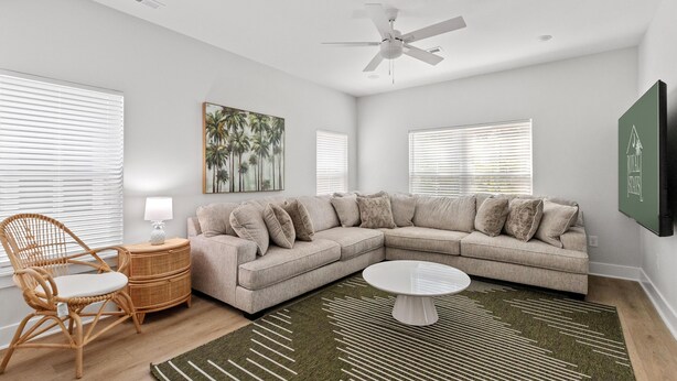 A modern living room with a sectional sofa, a round coffee table, a rattan chair, and a ceiling fan. - Pink Palmetto 2.5 Blocks to Beach Pets (Myrtle Beach)