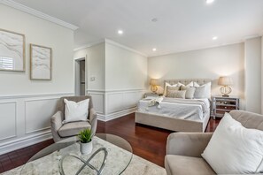 A spacious bedroom with a large bed, two bedside tables with lamps, a seating area with a chair and a small table, and a potted plant. - Luxurious townhome ideal for families, business travelers, and long stays. (Toronto)