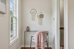 A room with a window, a wall-mounted macrame decoration, a small table with a vase, and a chair with a blanket. - Luxurious townhome ideal for families, business travelers, and long stays. (Toronto)