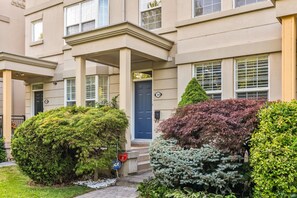A multi-story residential building with a central entrance, numbered doors, and a well-maintained garden with various shrubs. - Luxurious townhome ideal for families, business travelers, and long stays. (Toronto)