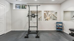 Un gimnasio en casa con una barra de dominadas, un soporte para pesas y un carrito azul con pesas.