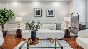 Una sala de estar moderna con un sofá blanco, dos mesitas de noche con lámparas, una mesa de centro con un jarrón y dos cuadros enmarcados en la pared.