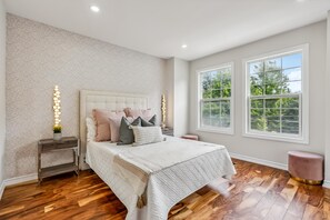 A bedroom with a large bed, two bedside tables, a nightstand, a window with a view of trees, and a patterned wall. - Luxurious townhome ideal for families, business travelers, and long stays. (Toronto)