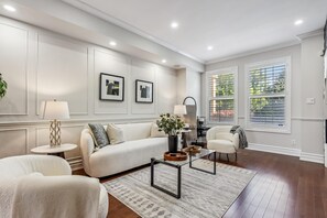 A modern living room with a sectional sofa, a coffee table, and a side table. There are two framed artworks on the wall, a window with blinds, and a plant on the side table. - Luxurious townhome ideal for families, business travelers, and long stays. (Toronto)