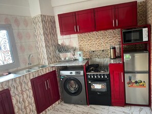 Una cucina funzionale con mobili rossi, lavatrice, fornello, microonde e frigorifero.