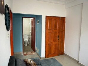 Een woonkamer met een bank, een houten deur en uitzicht op een badkamer.