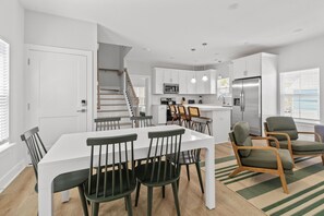 A modern kitchen with white cabinetry, a stainless steel refrigerator, and a dining area with a white table and chairs. - The Golden Tee - Pet Friendly-2.5 Blocks to Beach (Myrtle Beach)