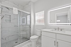 Ein modernes Badezimmer mit einer gläsernen Duschkabine, einer Toilette und einem Waschtisch mit Spiegel.