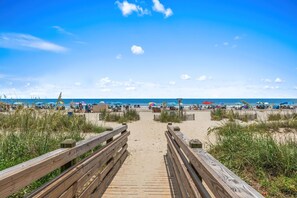 A wooden boardwalk leading to a beach with umbrellas and people. - The Golden Tee - Pet Friendly-2.5 Blocks to Beach (Myrtle Beach)